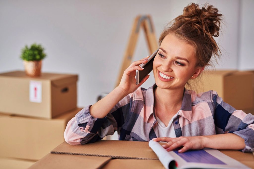 Happy woman calling removalist company with boxes packed in the background